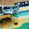 Broken PS5 HDMI port being pulled from a motherboard with tweezers
